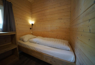 Habitación pequeña y acogedora con paredes de madera y cama individual en Drentse kap, EuroParcs Ruinen, Países Bajos.