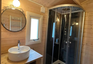 Bagno rivestito in legno con lavandino, specchio tondo e doccia moderna al Drentse kap, EuroParcs Ruinen, Paesi Bassi.