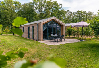 Außenansicht der Forest Lodge mit Terrasse, Gartenmöbeln, Sonnenschirm und viel Grün um das Haus.