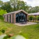 Forest Lodge eksteriør med terrasse, havemøbler og parasol, omgivet af grønne træer og græsplæne.