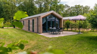 Außenansicht der Forest Lodge mit Terrasse, Gartenmöbeln, Sonnenschirm und viel Grün um das Haus.