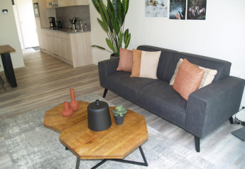 Salon du Forest Lodge à EuroParcs Ruinen avec canapé gris, table en bois, plantes et décoration moderne.