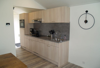 Moderne Küche in der Forest Lodge im EuroParcs Ruinen, Niederlande, mit Holzschränken und Wanduhr.