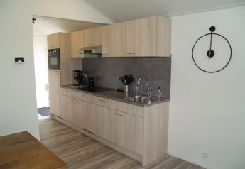 Moderne Küche in der Forest Lodge im EuroParcs Ruinen, Niederlande, mit Holzschränken und Wanduhr.
