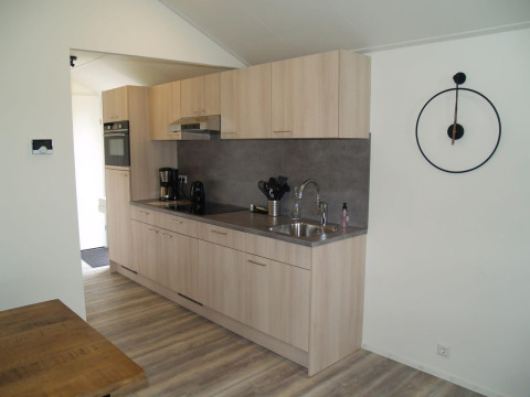 Interno cucina moderna presso Forest Lodge a EuroParcs Ruinen, Olanda, con mobili in legno e orologio a parete.