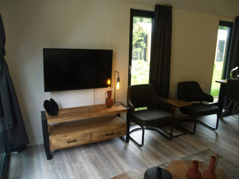Modernes Wohnzimmer mit Flachbildfernseher, bequemen Stühlen und großen Fenstern in der Forest Lodge.