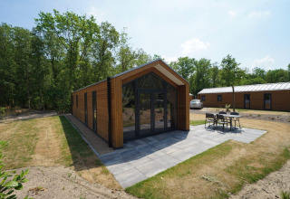 Forest Lodge ved EuroParcs Ruinen i Holland, omgivet af træer med terrasse og havemøbler foran.