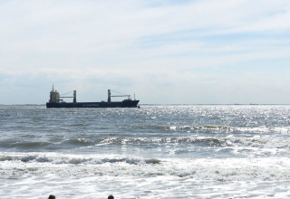 Tre børn leger i sandet ved stranden med et skib i baggrunden ved Dishoek i Zeeland, Holland.