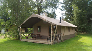 Vue extérieure de la Four Season Lodge avec terrasse couverte, table de pique-nique et verdure autour.
