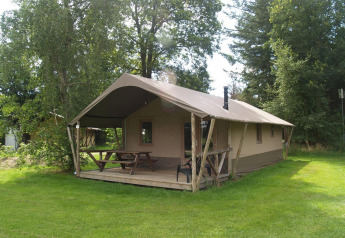 Vue extérieure de la Four Season Lodge avec terrasse couverte, table de pique-nique et verdure autour.