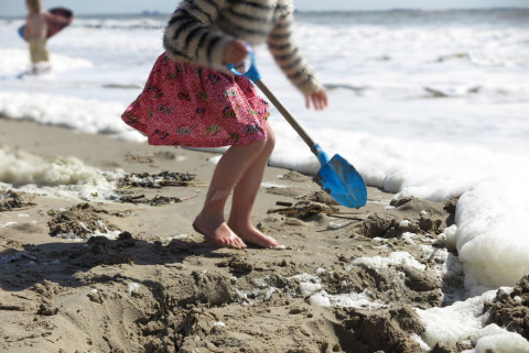 Een kind graaft met een blauwe schop in het zand aan het strandhuis 'Dishoek 60' in Zeeland, Nederland.