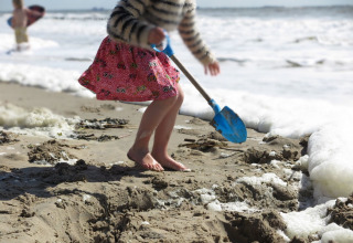 Un enfant creuse dans le sable avec une pelle bleue sur la plage près de Beach house 'Dishoek 60' à Zeeland, Pays-Bas.