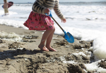 Een kind graaft met een blauwe schop in het zand aan het strandhuis 'Dishoek 60' in Zeeland, Nederland.