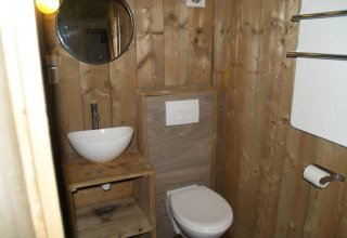 Baño de madera con lavabo, espejo y váter en Four Season Lodge en EuroParcs Ruinen, Países Bajos.