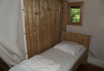 Paredes de madera y una cama individual con ropa de cama blanca en Four Season Lodge, EuroParcs Ruinen.