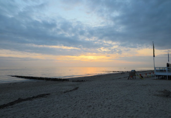 Solnedgang over stranden ved Beach house 'Dishoek 60' i Zeeland, Nederlandene, med stille hav og skyer.