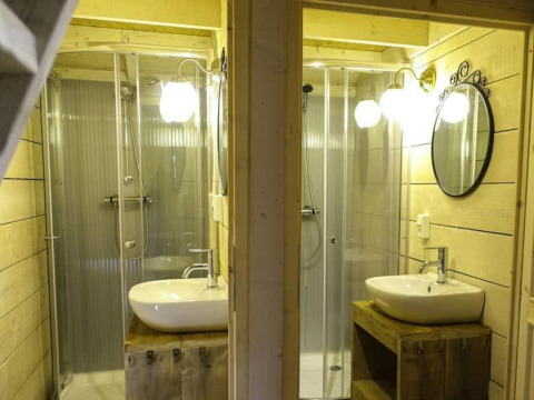 Dos baños idénticos con ducha y lavabo en un entorno de madera en Glamping Family Lodge 10, EuroParcs Ruinen.