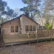 Træhytte ved Glamping Family Lodge 10 med terrasse, bænk og parasol i skovomgivelser, set udefra.
