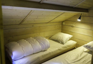 Due letti sotto un soffitto in legno inclinato con lampada da lettura nella Glamping family lodge 10, EuroParcs Ruinen.