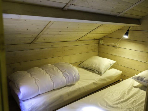 Deux lits sous un plafond en bois incliné avec lampe de lecture dans Glamping family lodge 10, EuroParcs Ruinen.