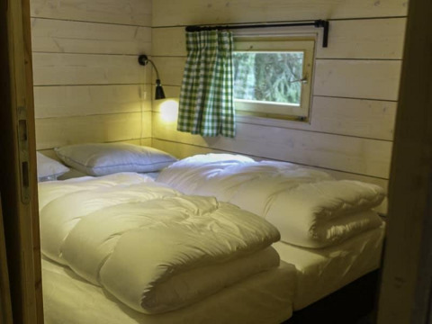 Dormitorio con cama doble, edredones blancos, cortina a cuadros verdes y paredes de madera en Glamping family lodge 10, EuroParcs Ruinen.
