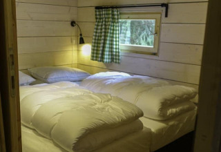 Camera da letto con letto matrimoniale, piumoni bianchi, tenda a quadretti verdi e pareti in legno alla Glamping family lodge 10, EuroParcs Ruinen.