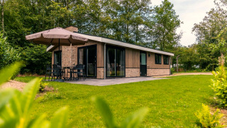 Outdoor view of the Hackfort chalet with patio, umbrella, and green garden surrounded by trees.