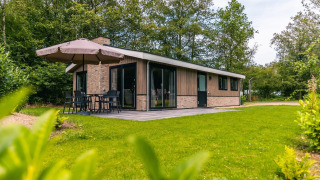 Buitenaanzicht van het Hackfort-chalet met terras, parasol en groene tuin tussen de bomen.