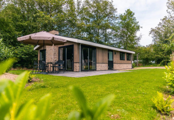 Buitenaanzicht van het Hackfort-chalet met terras, parasol en groene tuin tussen de bomen.