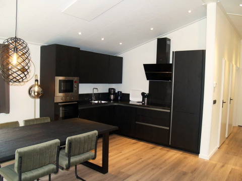 Modern dark kitchen in Hackfort chalet at EuroParcs Ruinen, Netherlands, featuring dining table and lighting.