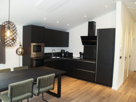 Cocina moderna oscura en chalet Hackfort de EuroParcs Ruinen, Países Bajos, con mesa y lámpara elegante.