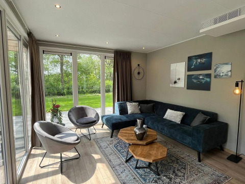 Moderne woonkamer met grote ramen, groen uitzicht en stijlvolle inrichting in chalet Hackfort bij EuroParcs Ruinen.