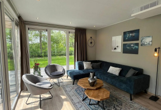Moderne woonkamer met grote ramen, groen uitzicht en stijlvolle inrichting in chalet Hackfort bij EuroParcs Ruinen.