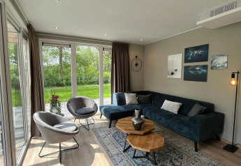 Moderne woonkamer met grote ramen, groen uitzicht en stijlvolle inrichting in chalet Hackfort bij EuroParcs Ruinen.