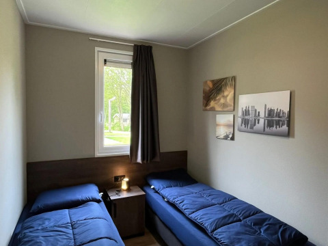 Chambre au chalet Hackfort d’EuroParcs Ruinen avec deux lits simples, tableaux au mur et fenêtre.
