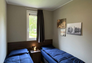Chambre au chalet Hackfort d’EuroParcs Ruinen avec deux lits simples, tableaux au mur et fenêtre.