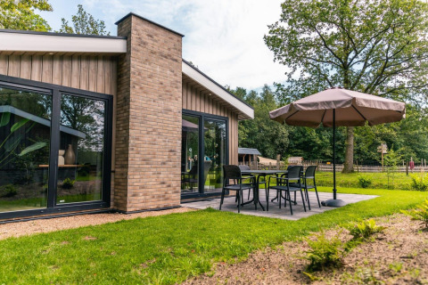 Modern chalet Hackfort bij EuroParcs Ruinen met terras, tuinset en grote parasol, midden in het groen.