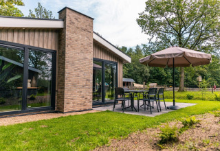 Modern chalet Hackfort bij EuroParcs Ruinen met terras, tuinset en grote parasol, midden in het groen.