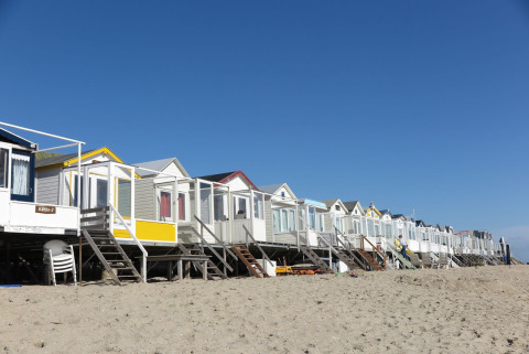Række strandhuse ved stranden under blå himmel, heriblandt Beach house 'Dishoek 60' med trapper.
