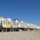 Række strandhuse ved stranden under blå himmel, heriblandt Beach house 'Dishoek 60' med trapper.