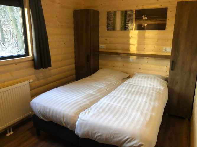 Schlafzimmer mit zwei Einzelbetten, Holzwänden, Fenster und Schränken in der Velthorst-Lodge De Wiltzangh, Niederlande.