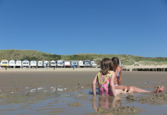 Deux enfants jouent dans le sable devant des maisons de plage à Dishoek 60, Zeeland, Pays-Bas, sous le soleil.