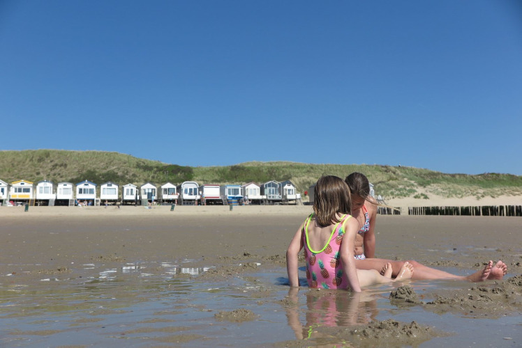 Zwei Kinder spielen am Sandstrand vor Strandhäusern in Dishoek 60, Zeeland, Niederlande, bei Sonnenschein.