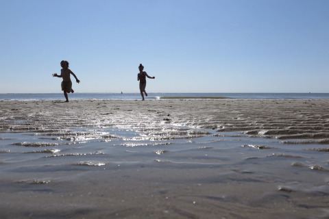 Kinder rennen und spielen am Strand bei Ebbe vor Beach house 'Dishoek 60' in Zeeland, Niederlande.