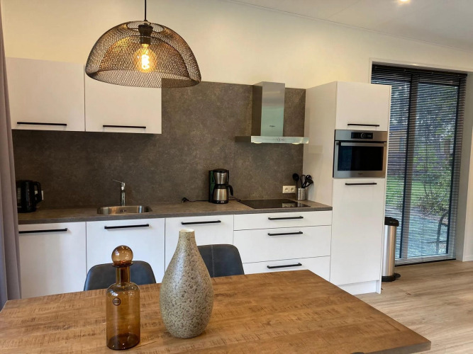 Modernes Lodge-Kücheninterieur mit weißen Schränken, Esstisch und Fenster mit Blick ins Grüne.