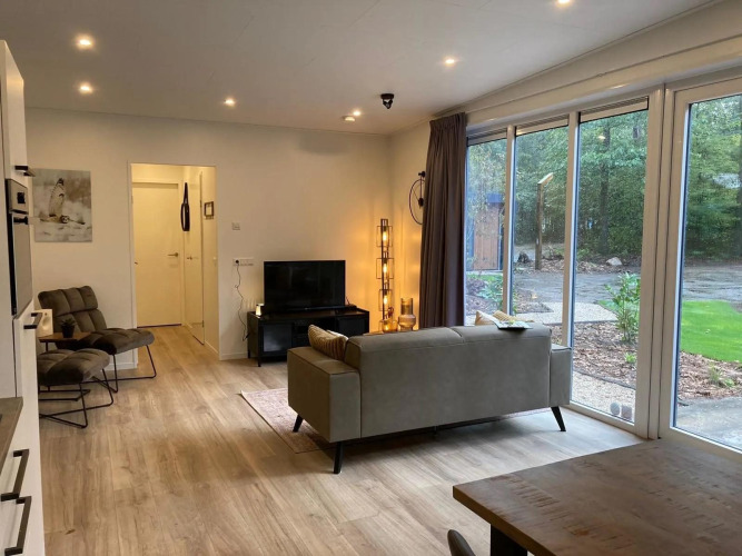 Modernes Wohnzimmer in einer Lodge mit großen Fenstern, bequemen Sesseln und Blick auf bewaldeten Garten.