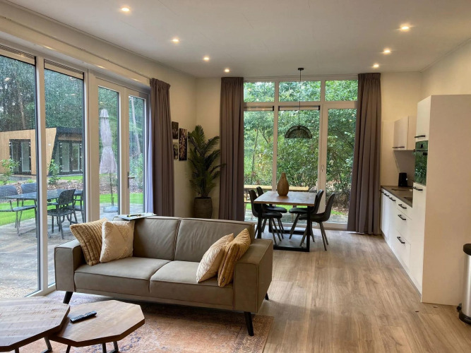 Moderne Lodge mit großen Fenstern, Wohnzimmer, Essbereich, Küche und Blick auf Terrasse und Garten.