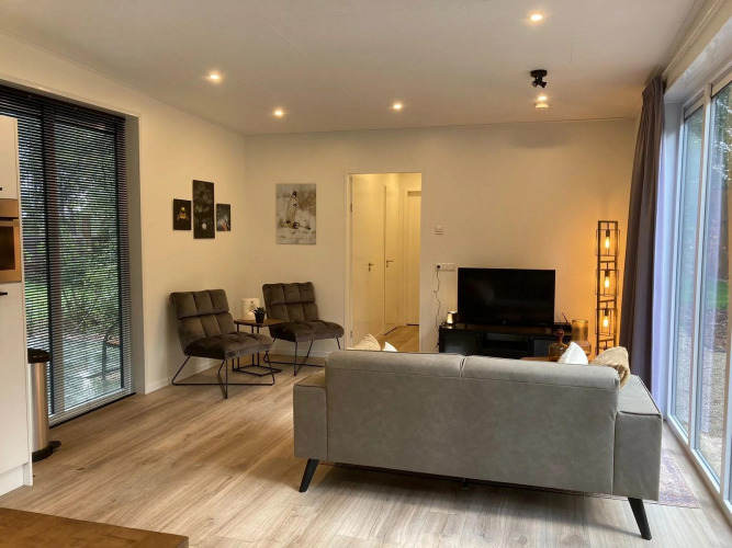 Modernes Wohnzimmer in einer Lodge mit grauem Sofa, zwei Sesseln, TV, großen Fenstern und Holzboden.