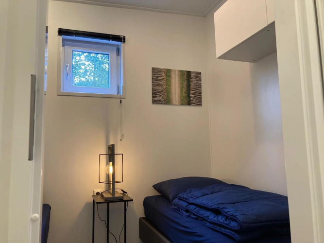 Gemütliches Zimmer in einer Lodge mit Einzelbett, Nachttischlampe, Fenster und Wandbild.