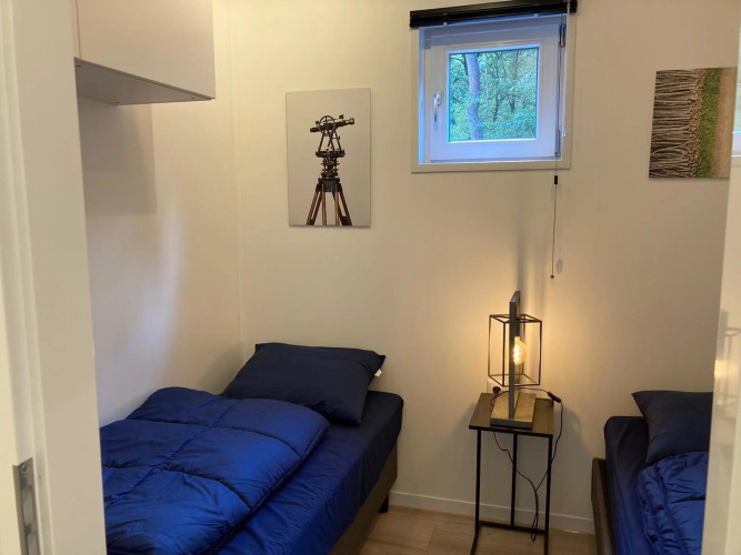 Ein kleines Lodge-Zimmer mit zwei Einzelbetten, blauer Bettwäsche, Fenster und moderner Lampe in der Mitte.